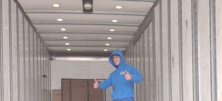Person in a blue jacket standing inside the back of a cargo truck with stacked boxes