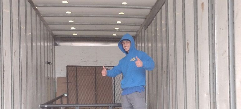 Person in a blue hoodie standing inside a truck trailer with cardboard boxes in the back.