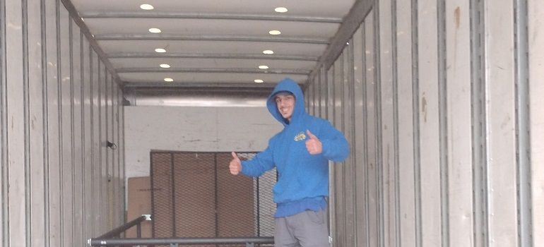 Person in a blue hoodie standing inside a semi-truck trailer giving two thumbs up