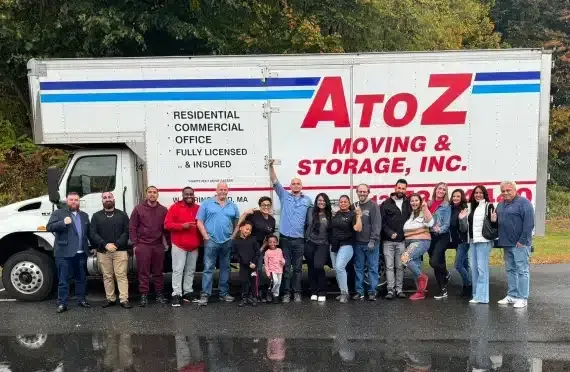 Group posing in front of ATOZ Moving & Storage truck on a wet street.