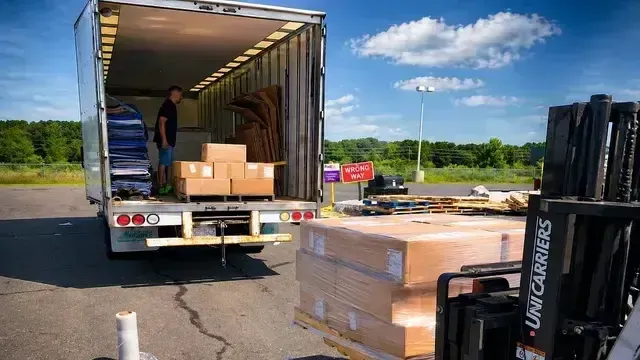 Open truck loading dock with pallets and boxes in a parking lot under a blue sky.