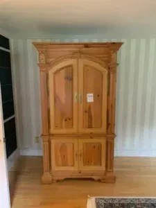 Wooden armoire with carved top in a light-colored room on hardwood floor
