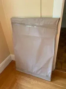 Gray padded moving bag leaning against a wall on a hardwood floor