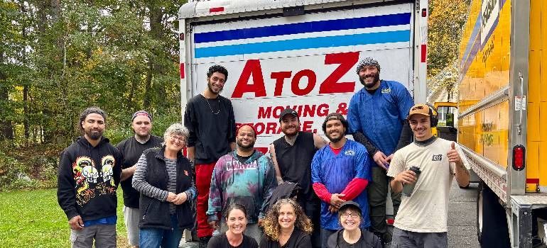 AtoZ Moving team poses in front of a moving truck in a grassy, wooded area.