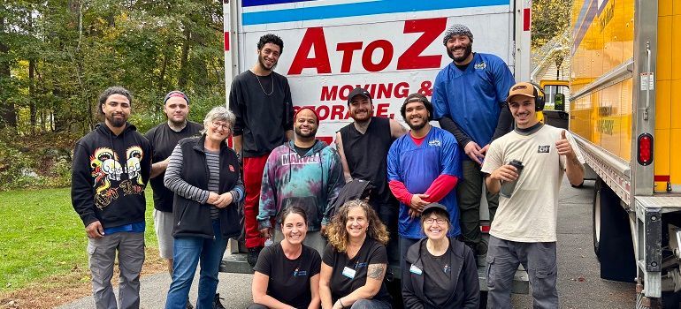Group of movers posing by a yellow truck with “AtoZ Moving” logo and red bins outdoors
