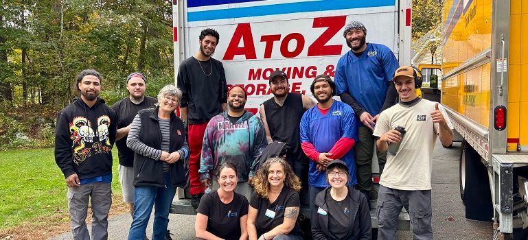 Group posing by AtoZ Moving & Storage truck, smiling on a tree-lined street