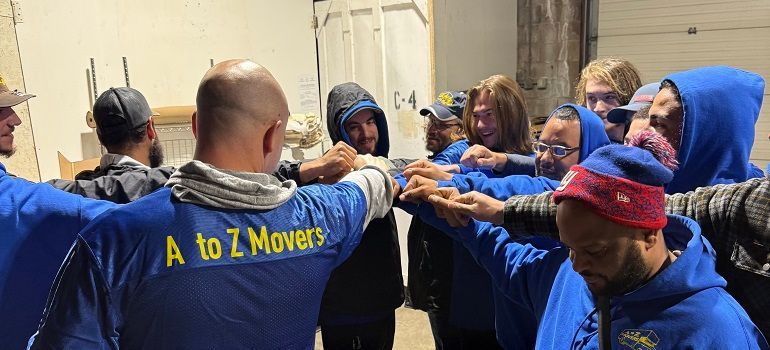 Team of movers in blue shirts celebrating with raised fists in a warehouse area