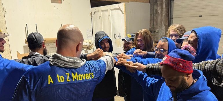 People in blue shirts stand in a circle with arms extended in a team huddle.