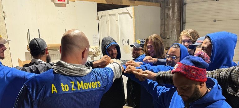 Group of people in blue hoodies with arms outstretched in a team huddle indoors