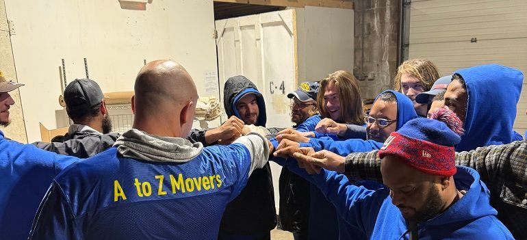 Movers in blue A to Z Movers shirts gather with arms outstretched in a warehouse loading area