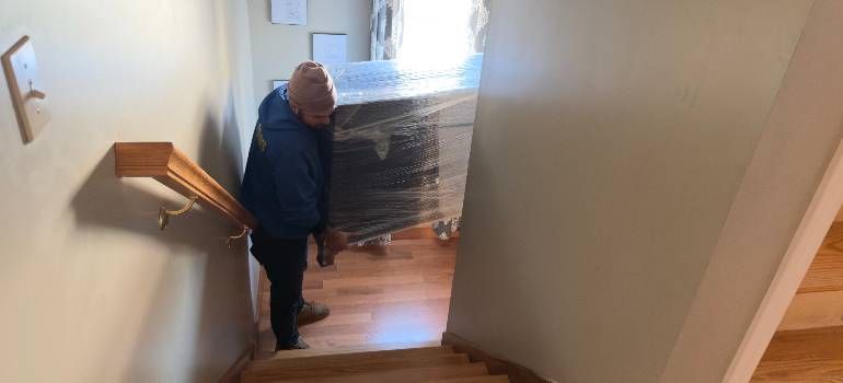Person standing on a staircase beside a wrapped item in a hallway