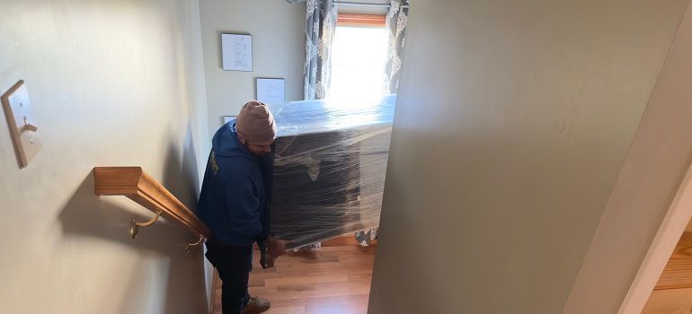 Mover carrying wrapped furniture down a narrow hallway