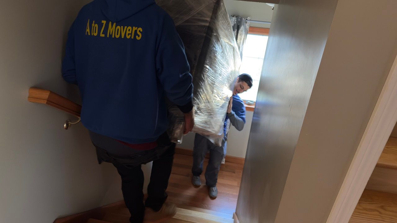 Two movers carry furniture down a narrow staircase in a house.