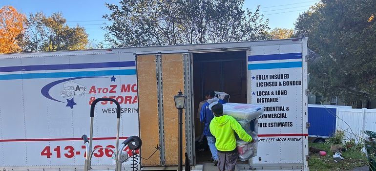 Workers loading a white truck with red and blue signage at an outdoor site