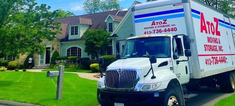White AtoZ moving truck parked in front of a suburban house on a sunny street