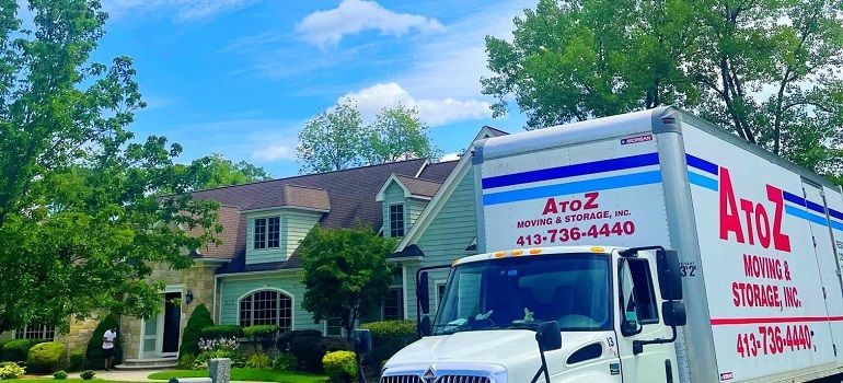 Azuz moving truck parked by a house in a leafy suburban neighborhood under a blue sky