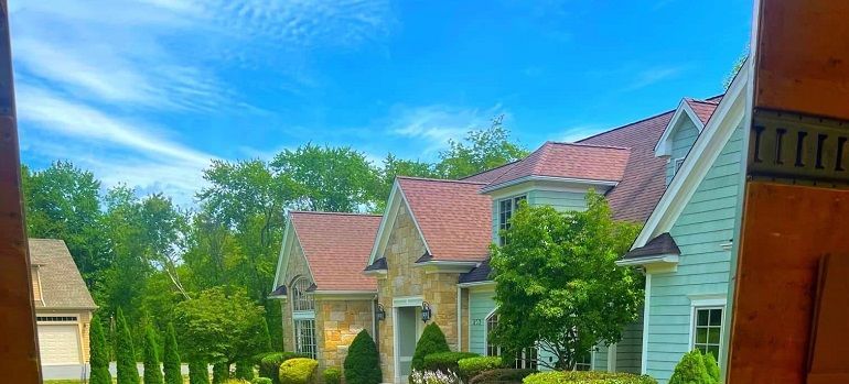 Sunlit suburban homes with red roofs, green trees, and a bright blue sky
