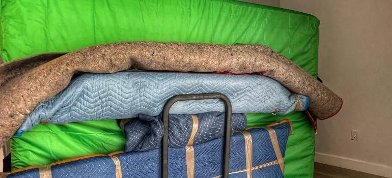 Stacked folded bedding and cushions on a blue cart, including a bright green blanket and blue pillows