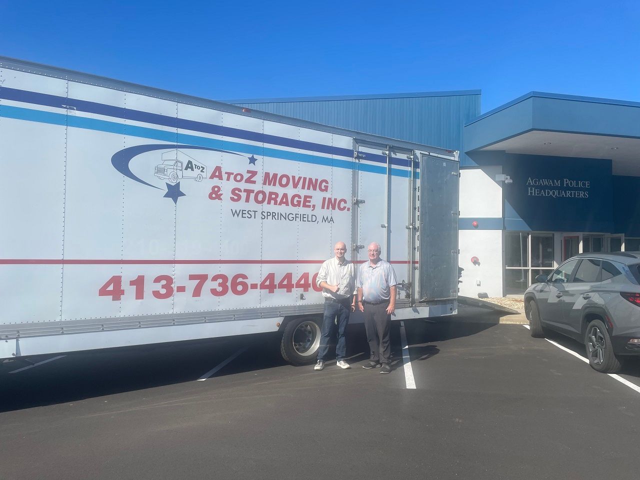 Two movers beside an Ariz Moving & Storage truck outside a warehouse loading dock