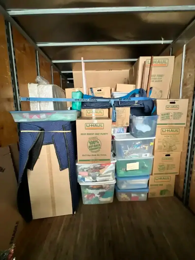 Packed moving truck with stacked cardboard boxes, storage bins, and furniture inside.