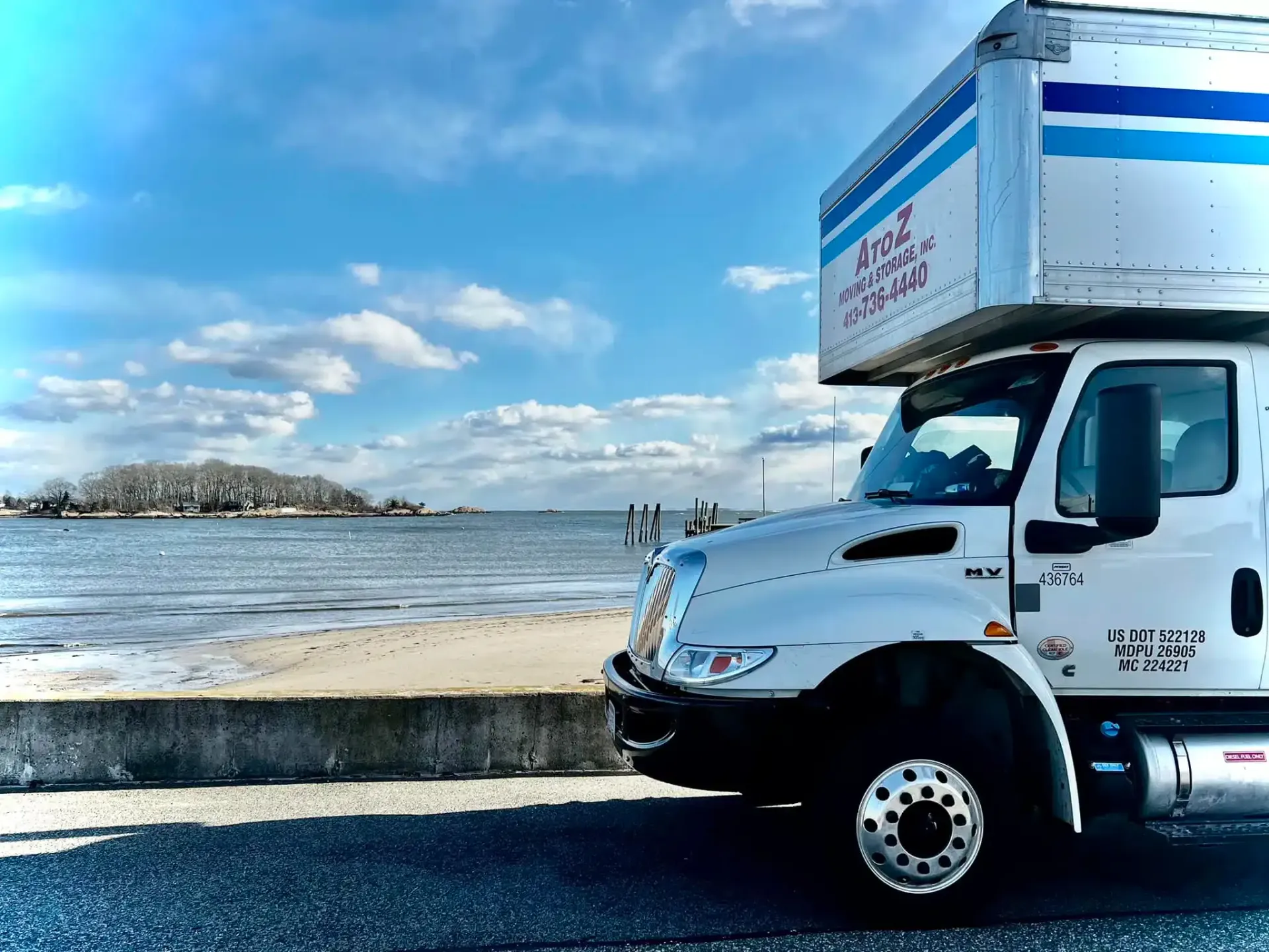 White box truck parked by a waterfront under a blue, cloudy sky