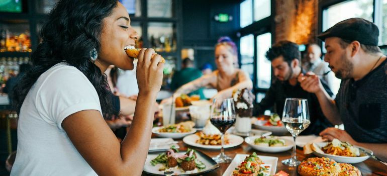 People sharing a meal at a restaurant table, with one woman eating and others chatting in the background