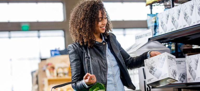 Woman shopping in a store aisle, reaching for an item on a shelf and holding a produce bag
