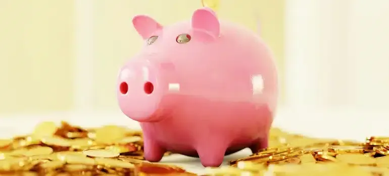Pink piggy bank sitting on gold coins, symbolizing savings and money.
