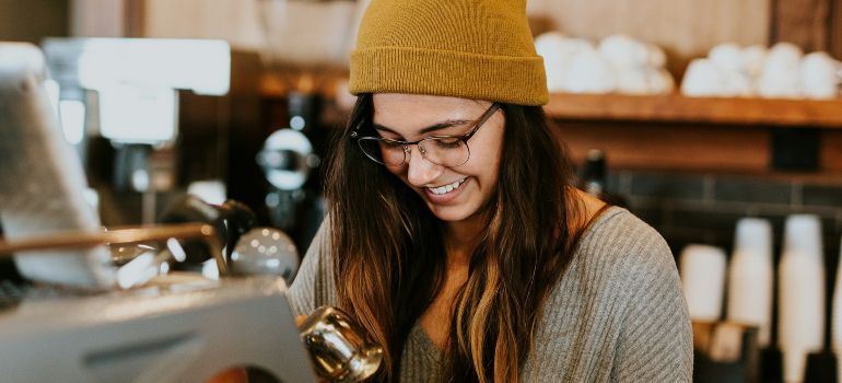 Smiling barista in a mustard beanie working behind a coffee shop counter