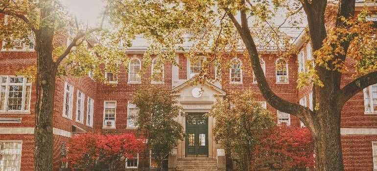 Red-brick building with white columns, framed by autumn trees and red ivy-covered walls