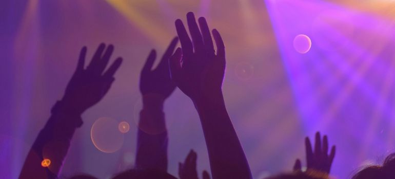 Silhouetted hands raised in a purple-lit concert crowd with stage lights in the background