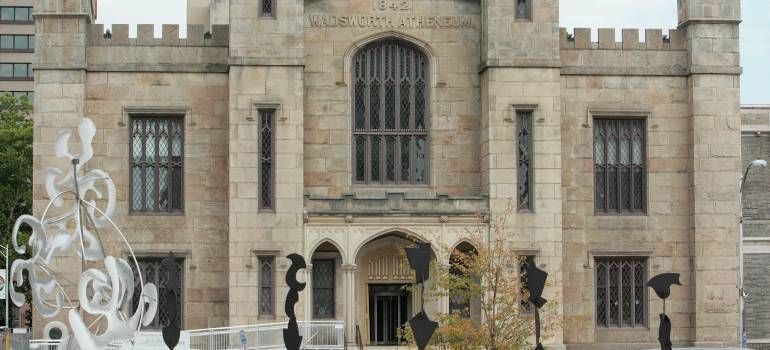 Stone castle facade with arched entrance, tall windows, and decorative white sculpture in front