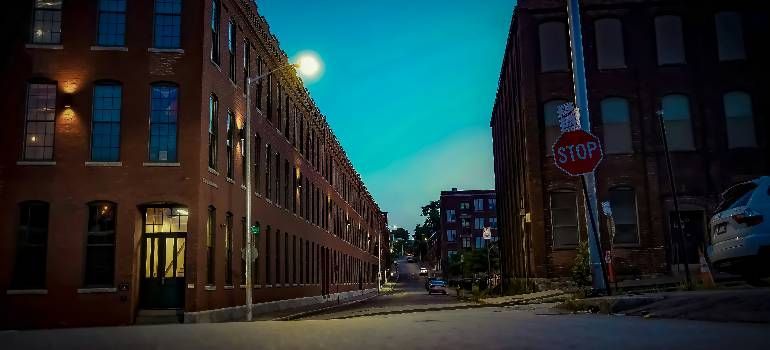 Dusk-lit empty city street between brick buildings, with a stop sign at the corner.