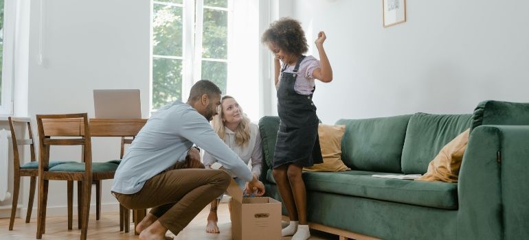 Two people unpacking boxes in a bright living room with a green sofa and wooden dining table
