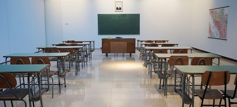 Empty classroom with rows of desks, chalkboard, and a teacher’s podium at the front.