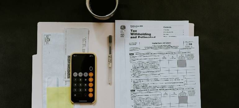 Desk with a phone, papers, and a pen next to a laptop and coffee cup