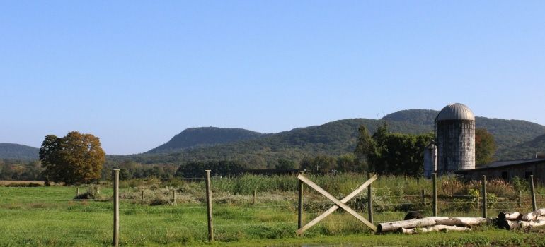 Rural field with fence, green hills, and a metal silo under a clear blue sky