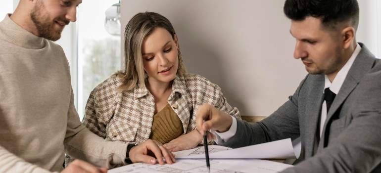 Three coworkers review documents at a table, one pointing with a pen during a meeting.