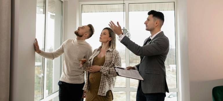 Three people discussing room layout in a bright office, with one man pointing upward