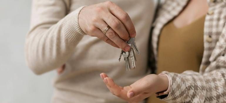 Person hands over keys to another person’s open palm indoors
