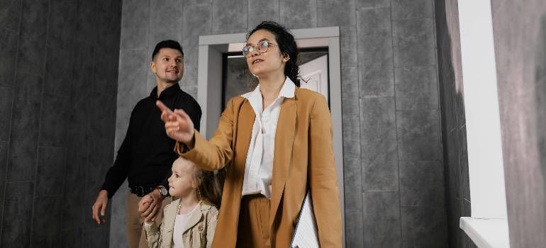 Three people in a hallway, one pointing ahead while the others look upward.