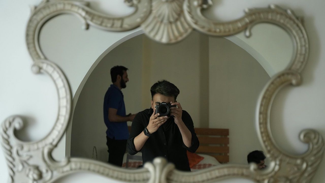 Person taking a mirror selfie in a decorative ornate frame, with another person standing in the background.
