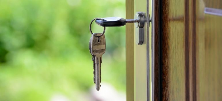 Keys hanging in a door lock on a wooden door, with a blurred green background