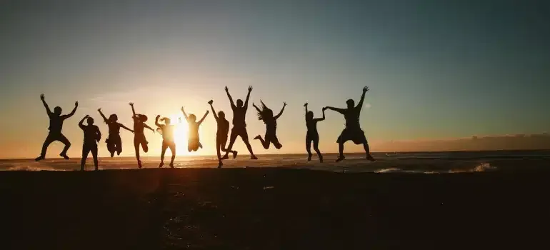 Silhouetted people jumping on a beach at sunset with arms raised