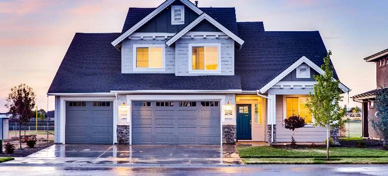 Modern two-story gray house with lit windows, a double garage, and a front porch at dusk