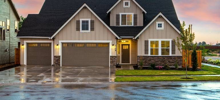 Modern suburban house with a dark roof, double garage, and wet driveway after rain