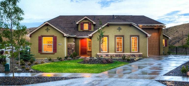 Single-story suburban house with warm lights, manicured lawn, and wet driveway at dusk