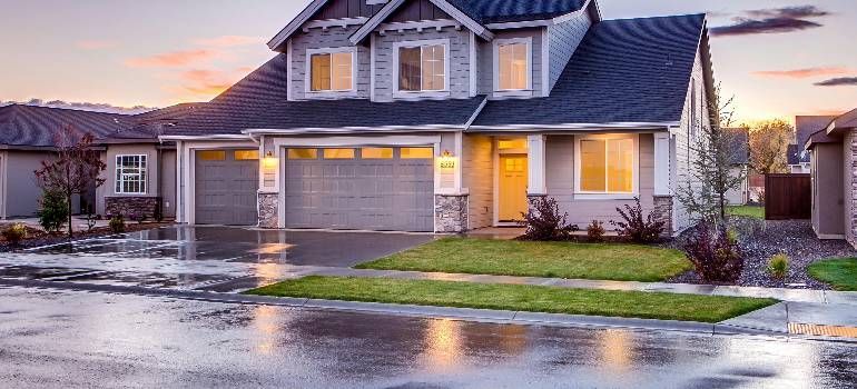 Suburban house with lit windows and wet driveway at dusk after rain