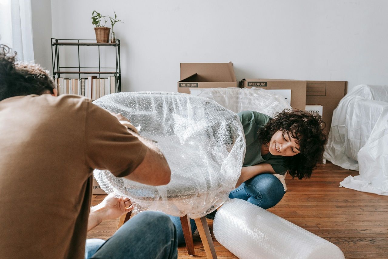 Two people wrapping a chair in bubble wrap in a bright living room