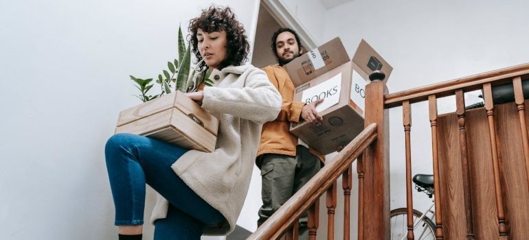 Two people carrying cardboard boxes up a staircase in a home moving scene